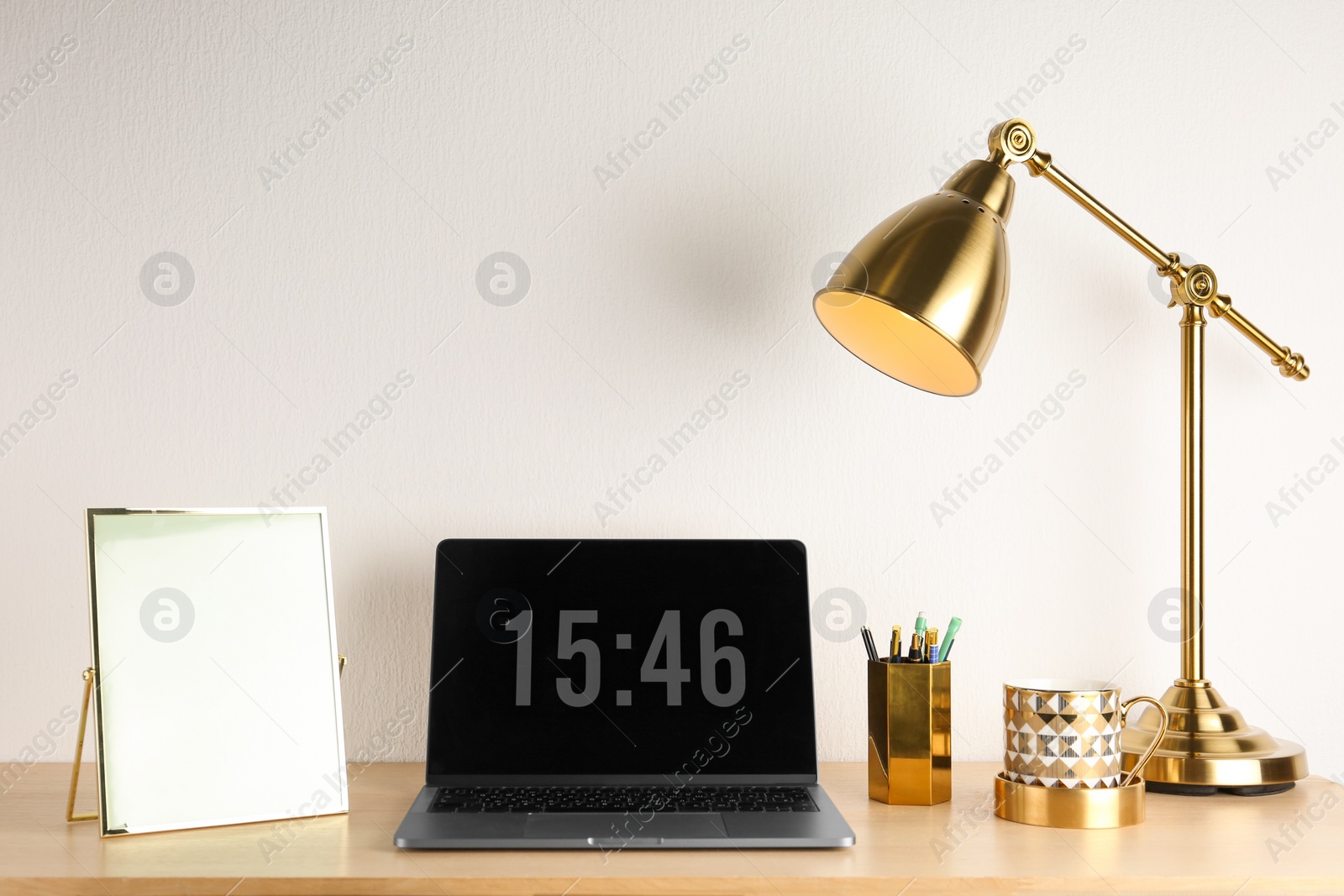 Photo of Modern workplace with laptop and golden decor on desk near wall. Stylish interior design