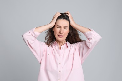 Mature woman suffering from headache on light grey background