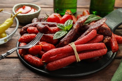 Photo of Different thin dry smoked sausages with basil on wooden table, closeup