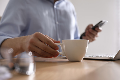 Photo of Man with cup of coffee at table indoors, closeup