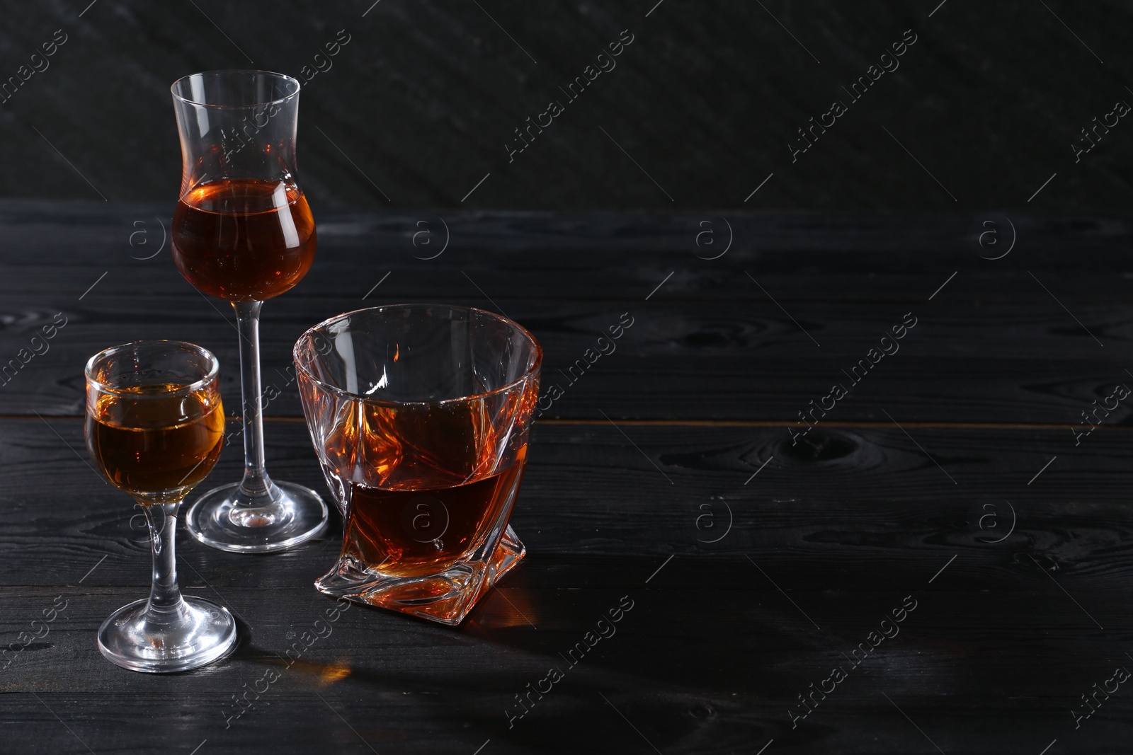 Photo of Different delicious liqueurs in glasses on black wooden table, space for text