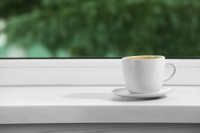 Cup of aromatic coffee on white sill near window indoors, space for text