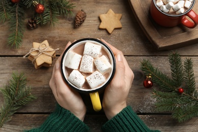 Photo of Woman with cup of delicious marshmallow cocoa at wooden table, top view