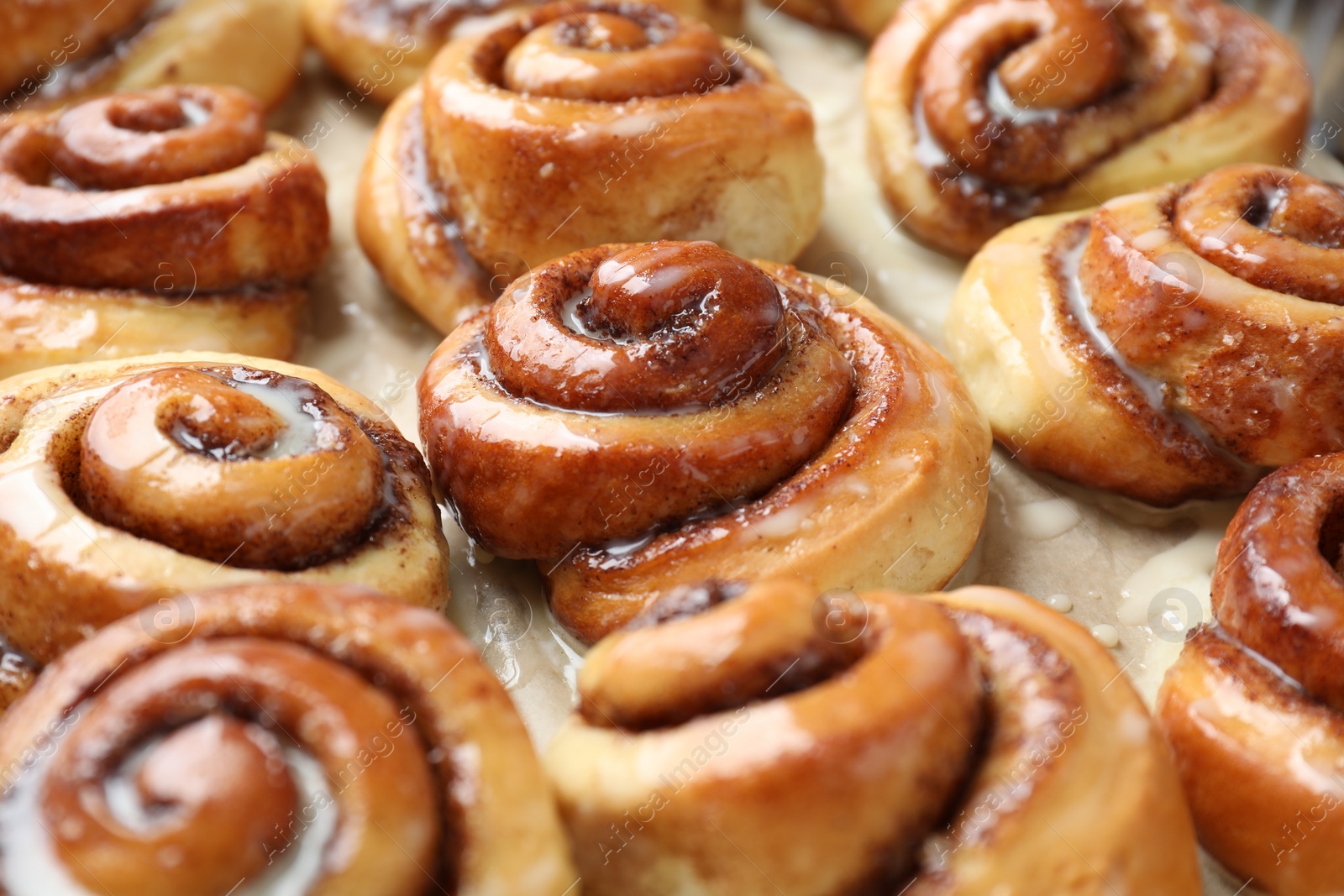 Photo of Tasty cinnamon rolls with cream on parchment paper, closeup