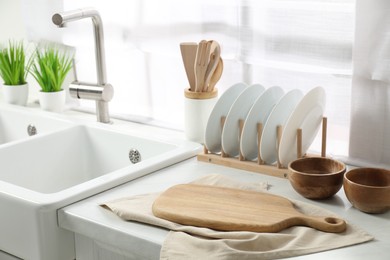 Photo of Wooden cutting board, dishware and towel on white countertop in kitchen