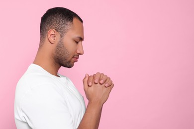 Photo of African American man with clasped hands praying to God on pink background. Space for text