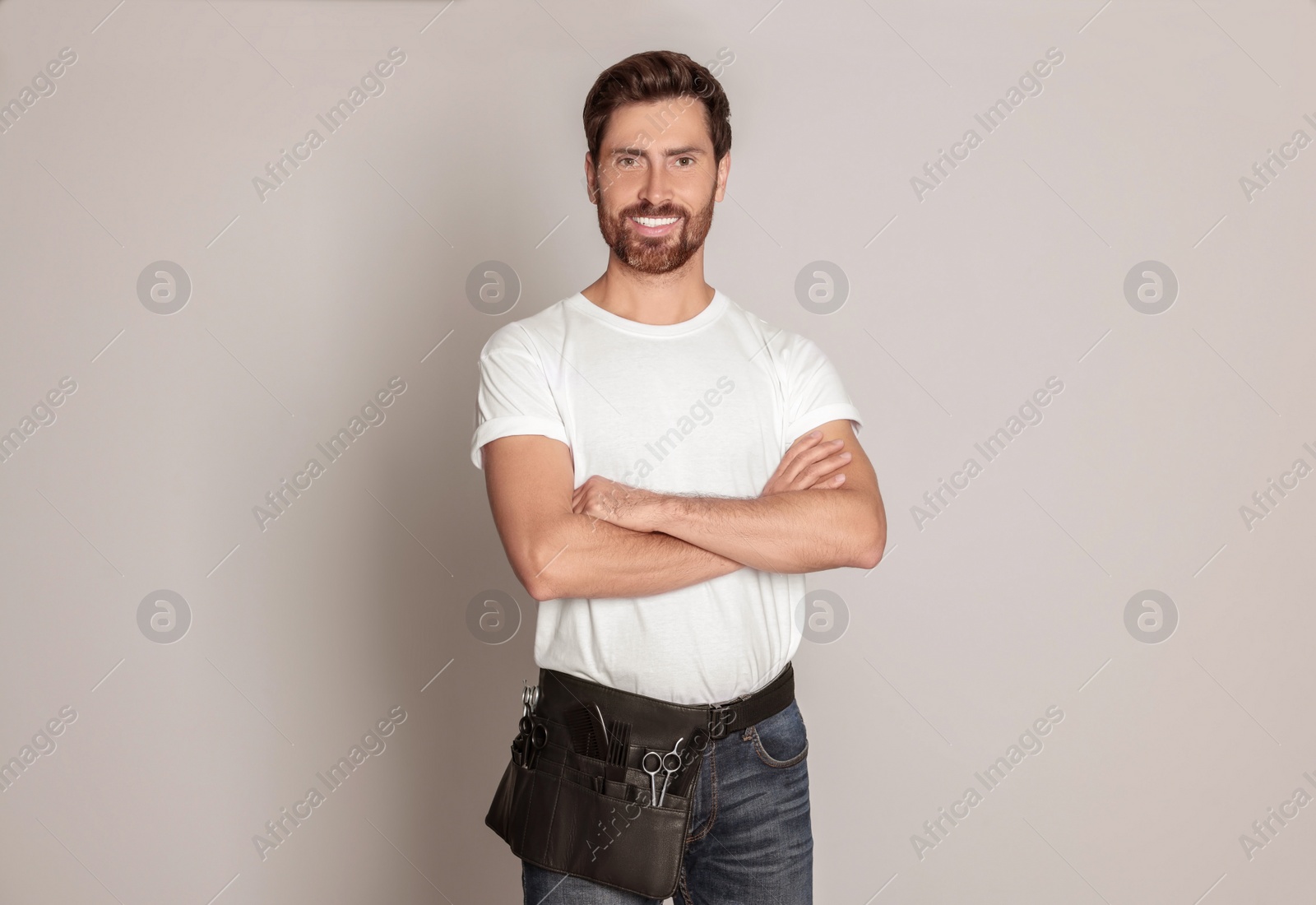 Photo of Smiling hairdresser with tool bag on light grey background