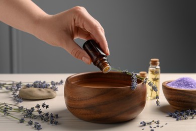 Woman dripping lavender essential oil from bottle into bowl at white wooden table, closeup. Space for text