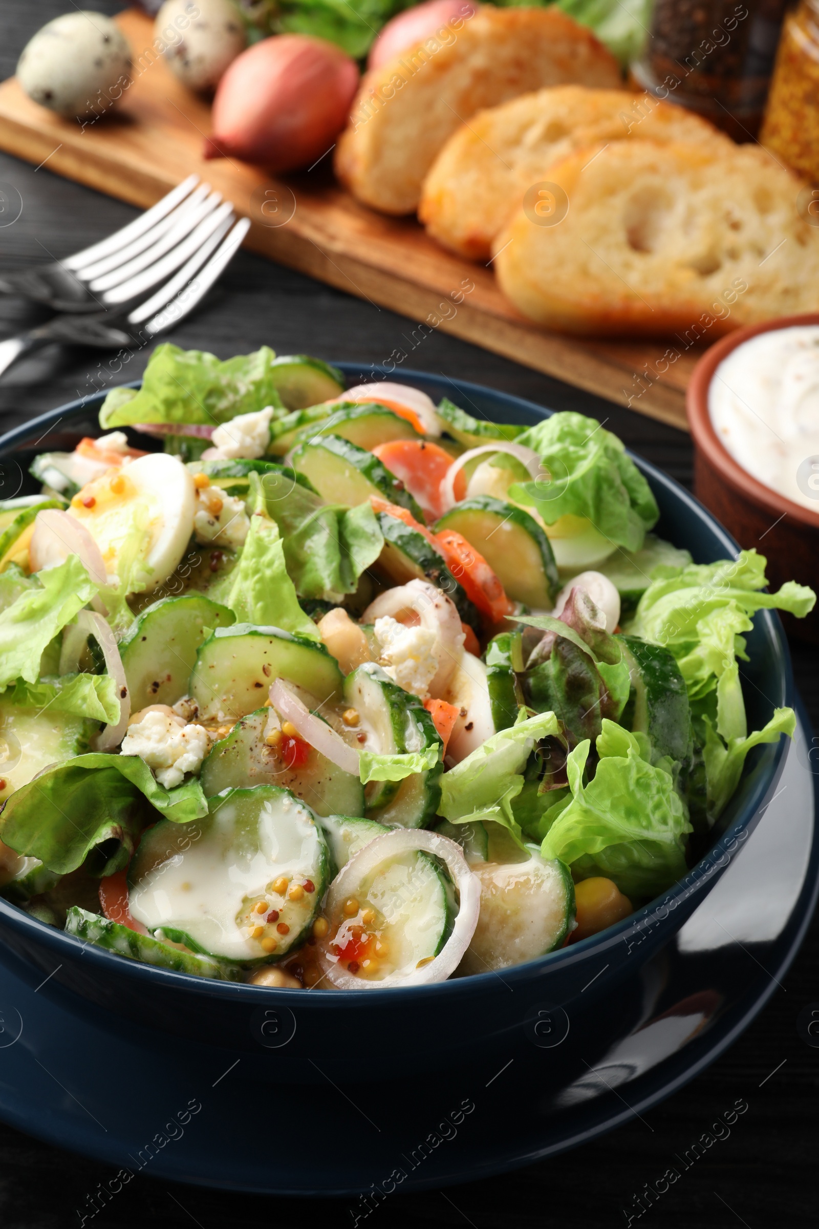 Photo of Bowl of delicious cucumber salad served on black table, closeup