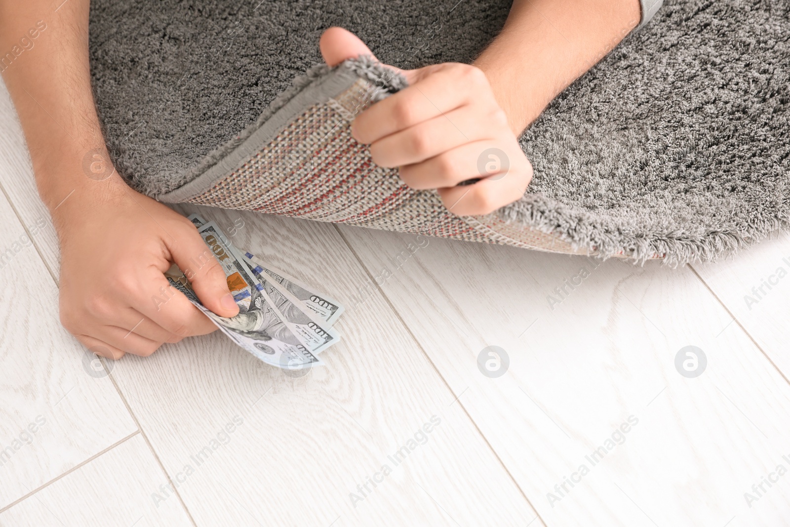 Photo of Man hiding money under carpet indoors, closeup. Financial savings