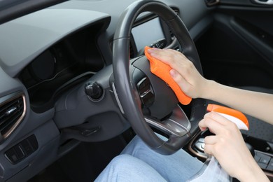 Photo of Woman cleaning steering wheel with rag in car, closeup