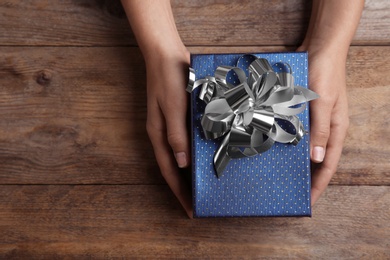 Photo of Woman holding beautiful gift box over wooden table, top view