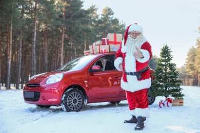 Photo of Authentic Santa Claus near red car with gift boxes and Christmas tree, outdoors