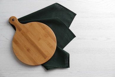 Empty wooden board and green napkin on white table, top view