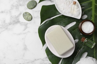 Flat lay composition with different spa products and tropical leaf on white marble table. Space for text