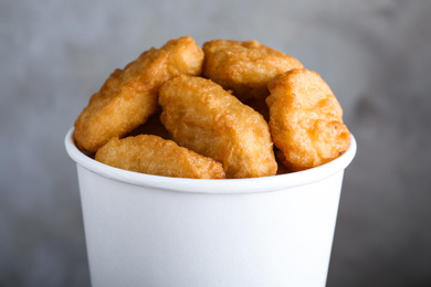 Photo of Bucket with delicious chicken nuggets on grey background, closeup