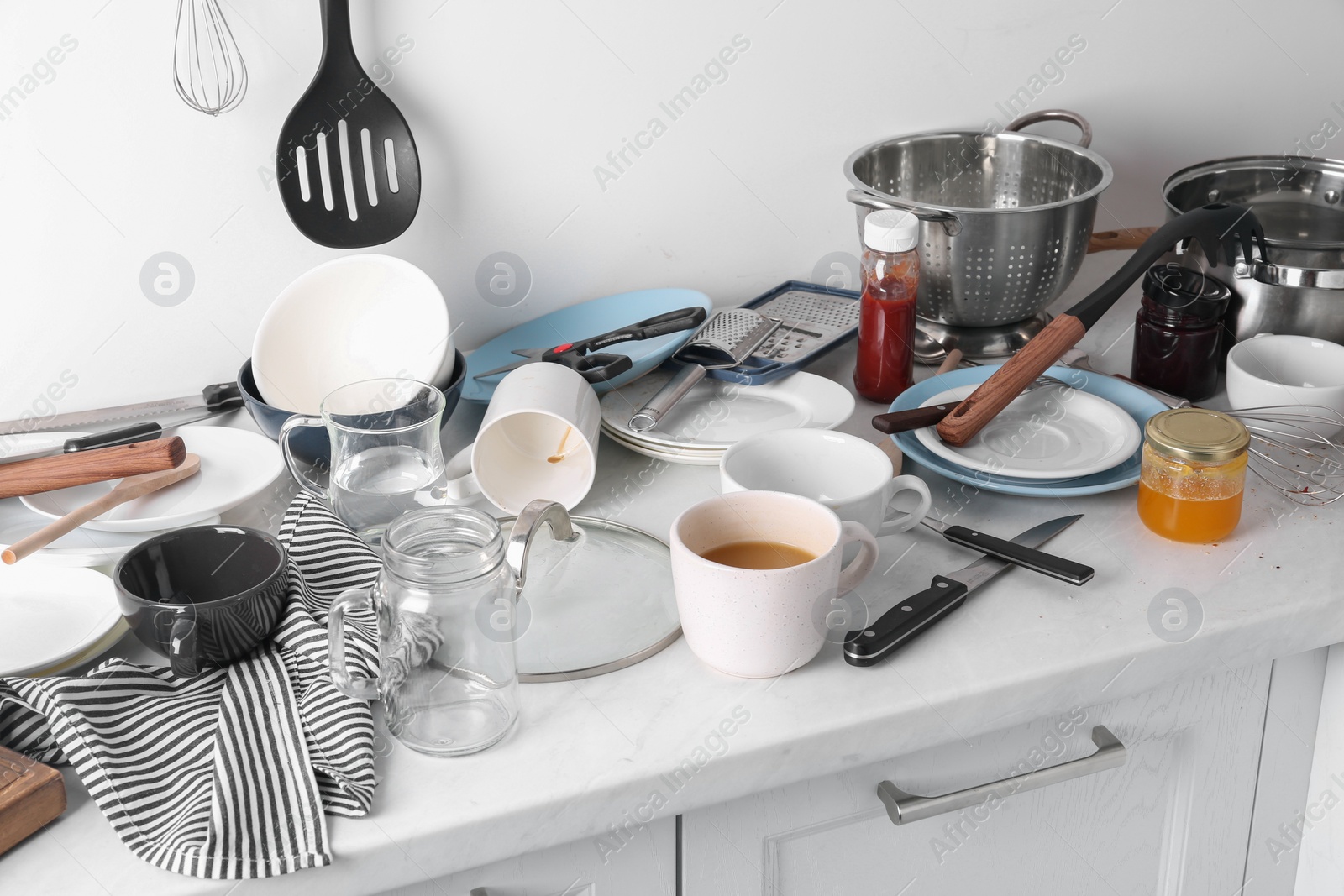 Photo of Many dirty utensils and dishware on countertop in messy kitchen