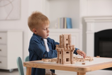 Cute little boy playing with wooden tower at table indoors, selective focus. Child's toy