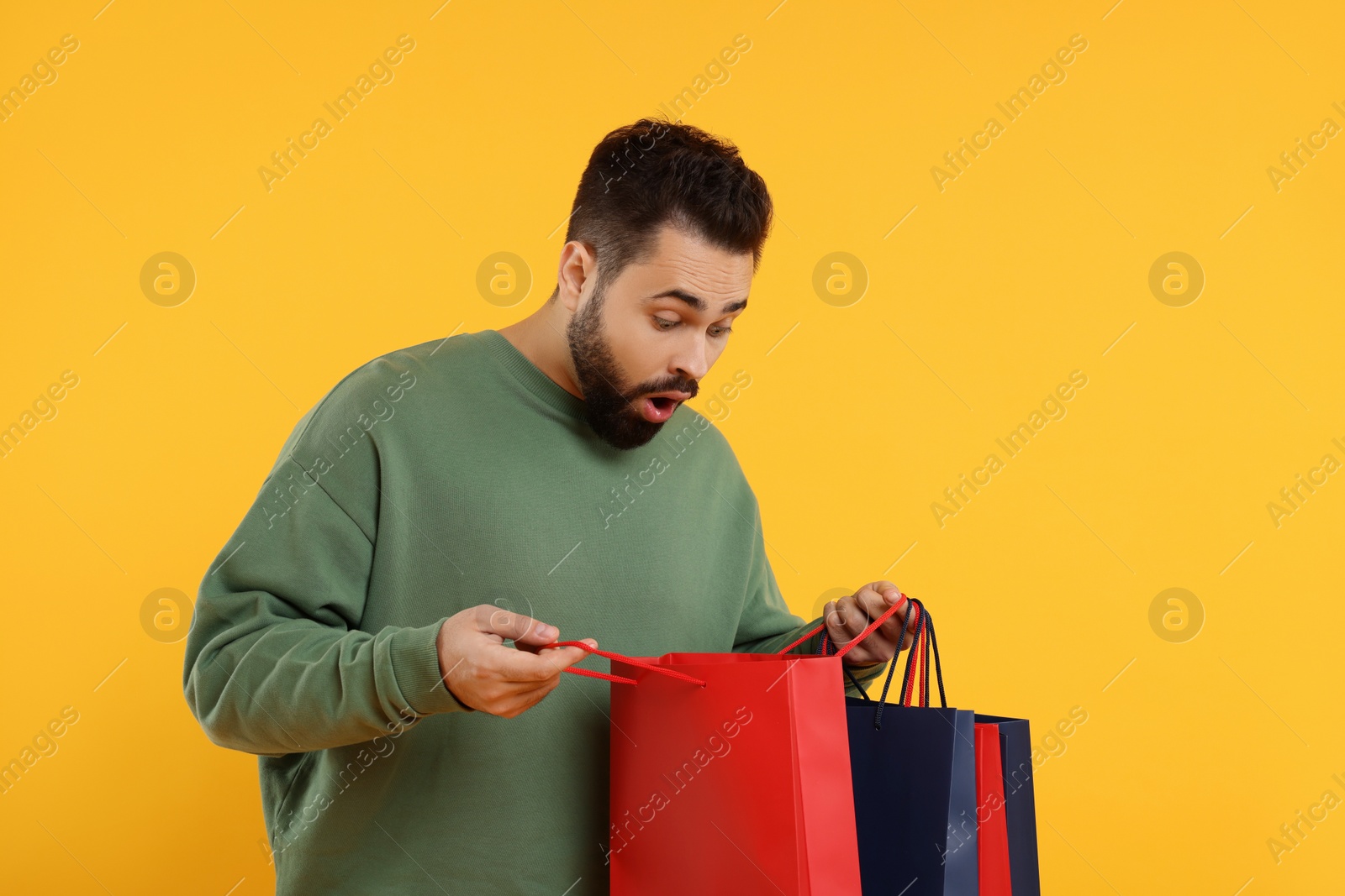 Photo of Excited man with many paper shopping bags on orange background