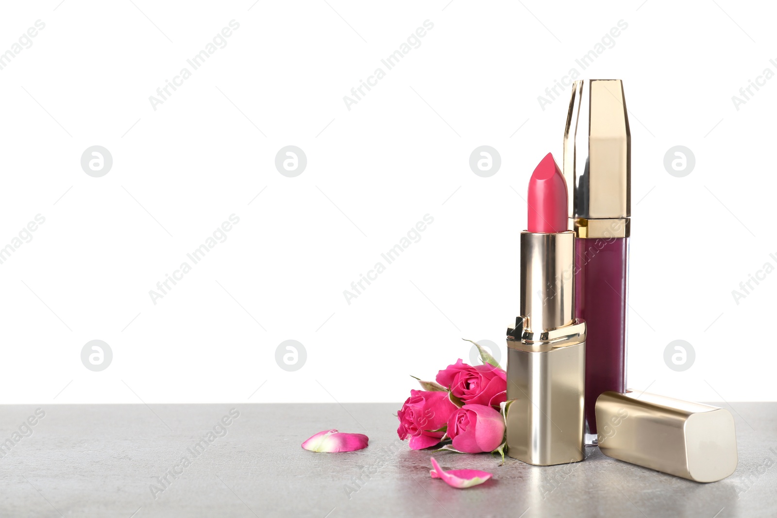 Photo of Lipstick and lipgloss with flowers on table against white background