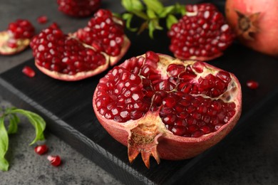 Photo of Cut fresh pomegranate and green leaves on grey table, closeup