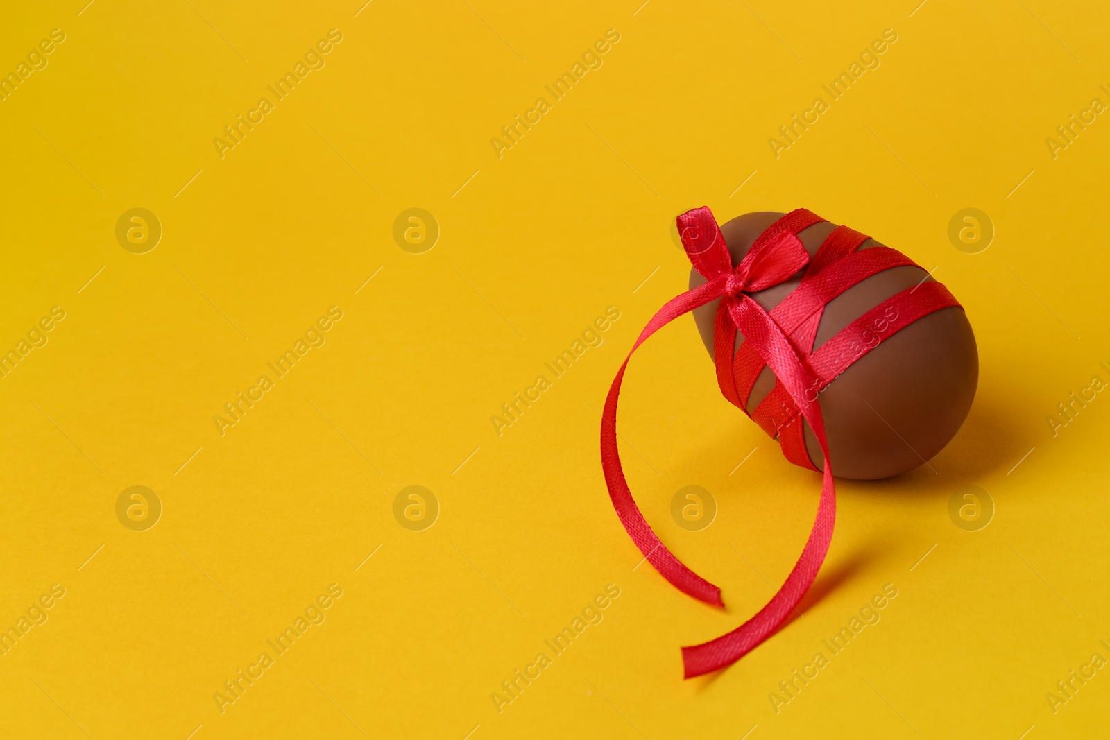 Photo of Tasty chocolate egg with red ribbon on orange background. Space for text