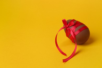 Photo of Tasty chocolate egg with red ribbon on orange background. Space for text