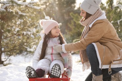 Photo of Young woman and her daughter with sledge outdoors on winter day. Christmas vacation