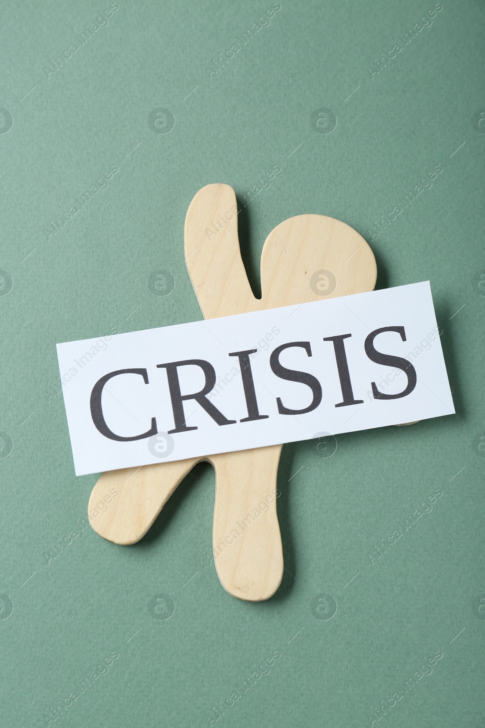 Photo of Wooden human figure and word Crisis on green background, top view