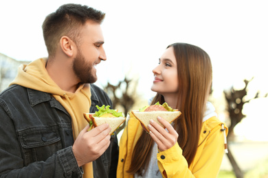 Photo of Happy young couple with sandwiches on city street