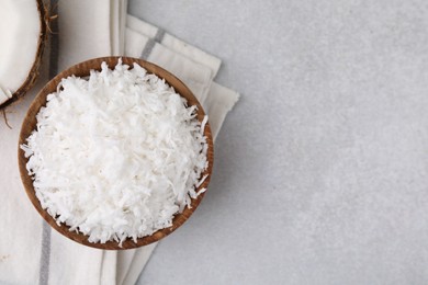 Coconut flakes in bowl on light grey table, top view. Space for text