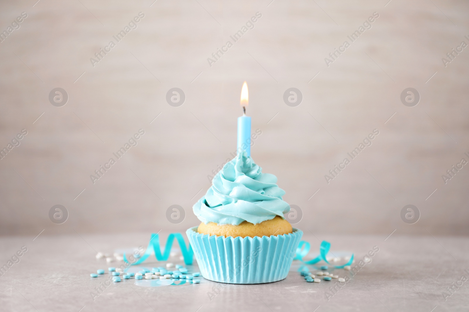 Photo of Delicious birthday cupcake with burning candle, sprinkles and streamer on grey table
