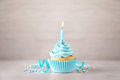 Delicious birthday cupcake with burning candle, sprinkles and streamer on grey table