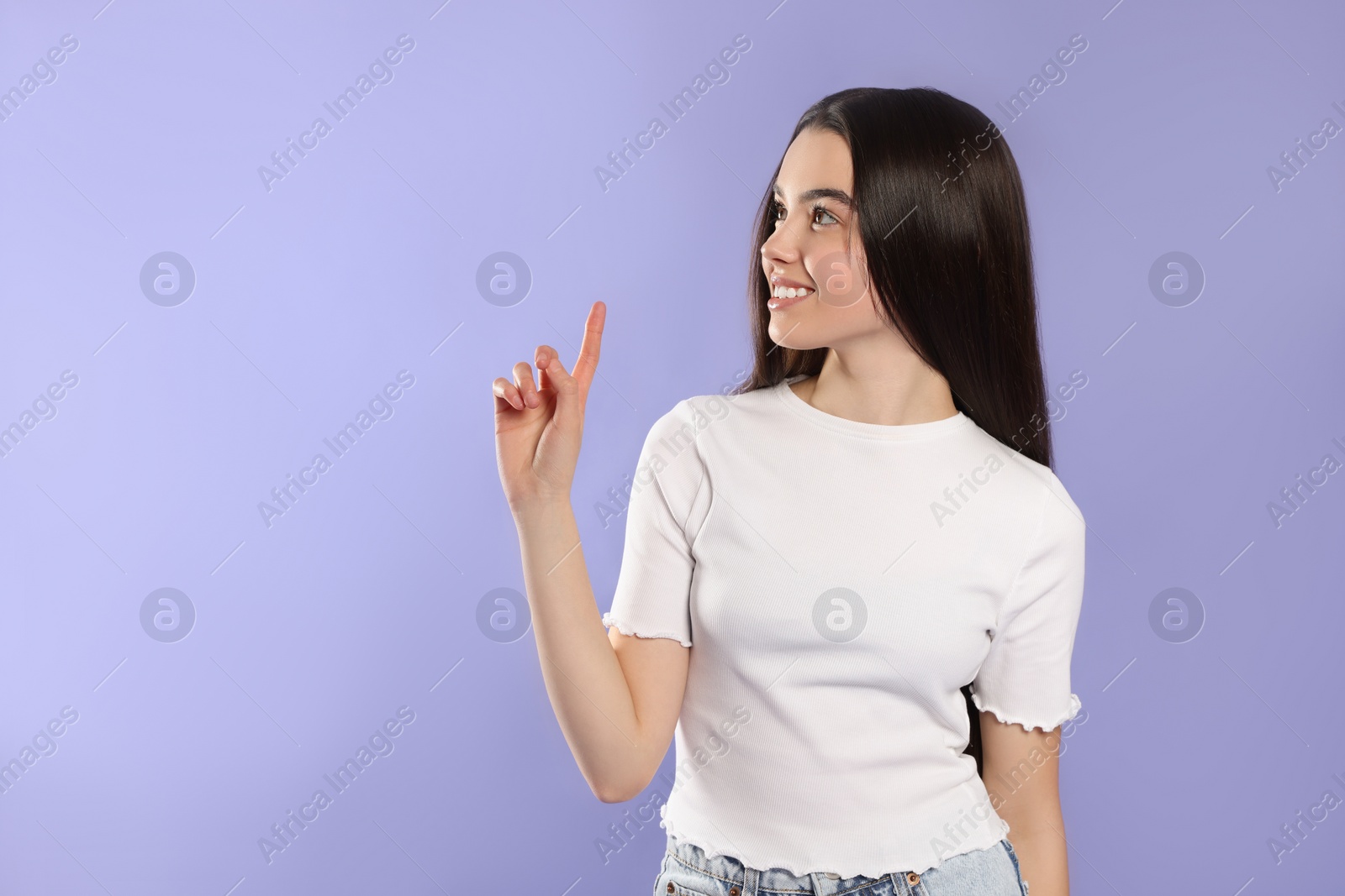 Photo of Teenage girl pointing at something on violet background. Space for text