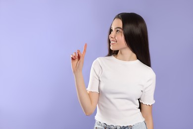 Photo of Teenage girl pointing at something on violet background. Space for text