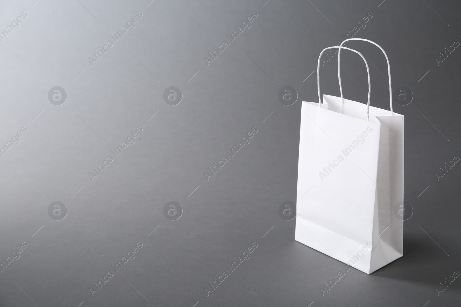 Photo of One white paper bag on grey background, space for text. Mockup for design