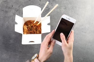 Photo of Woman with smartphone and Chinese noodles at grey table, space for text. Food delivery