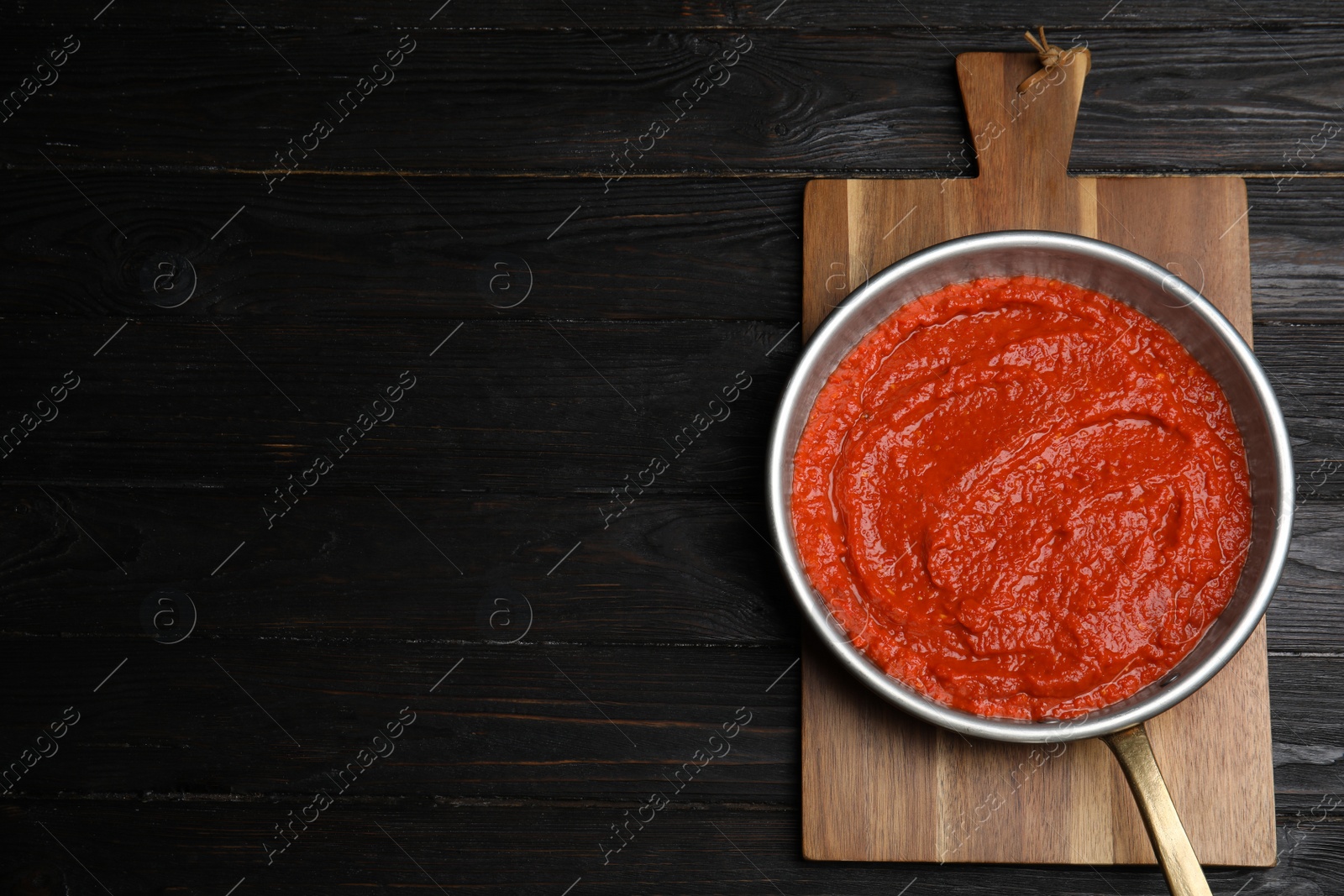 Photo of Delicious tomato sauce in pan on black wooden table, top view. Space for text