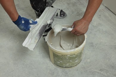 Photo of Professional worker taking plaster from bucket indoors, closeup