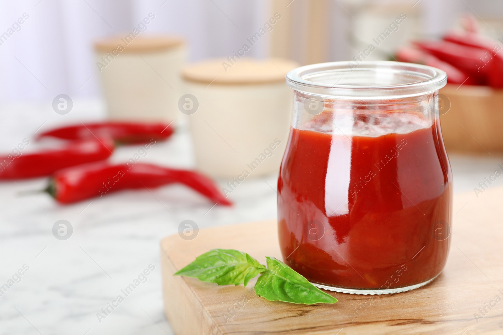 Photo of Jar with spicy chili sauce on marble table