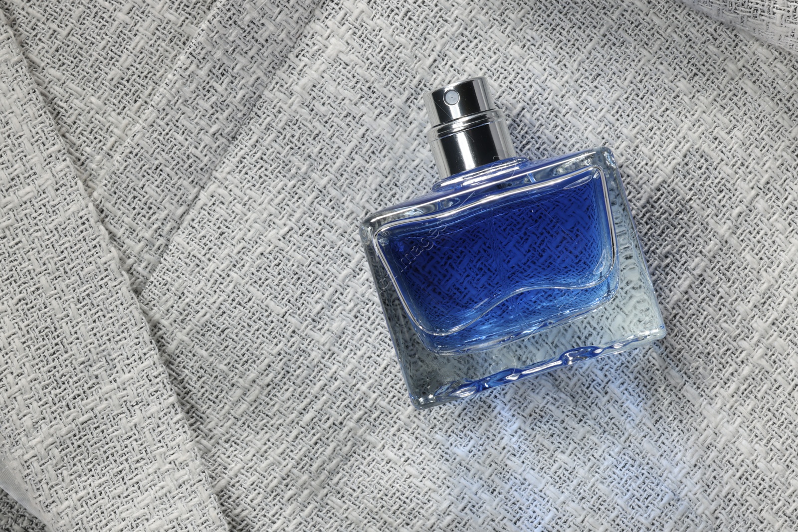 Photo of Luxury men's perfume in bottle on grey jacket, top view. Space for text