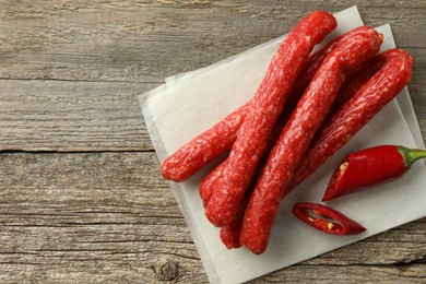 Photo of Thin dry smoked sausages and chili pepper on old wooden table, top view. Space for text