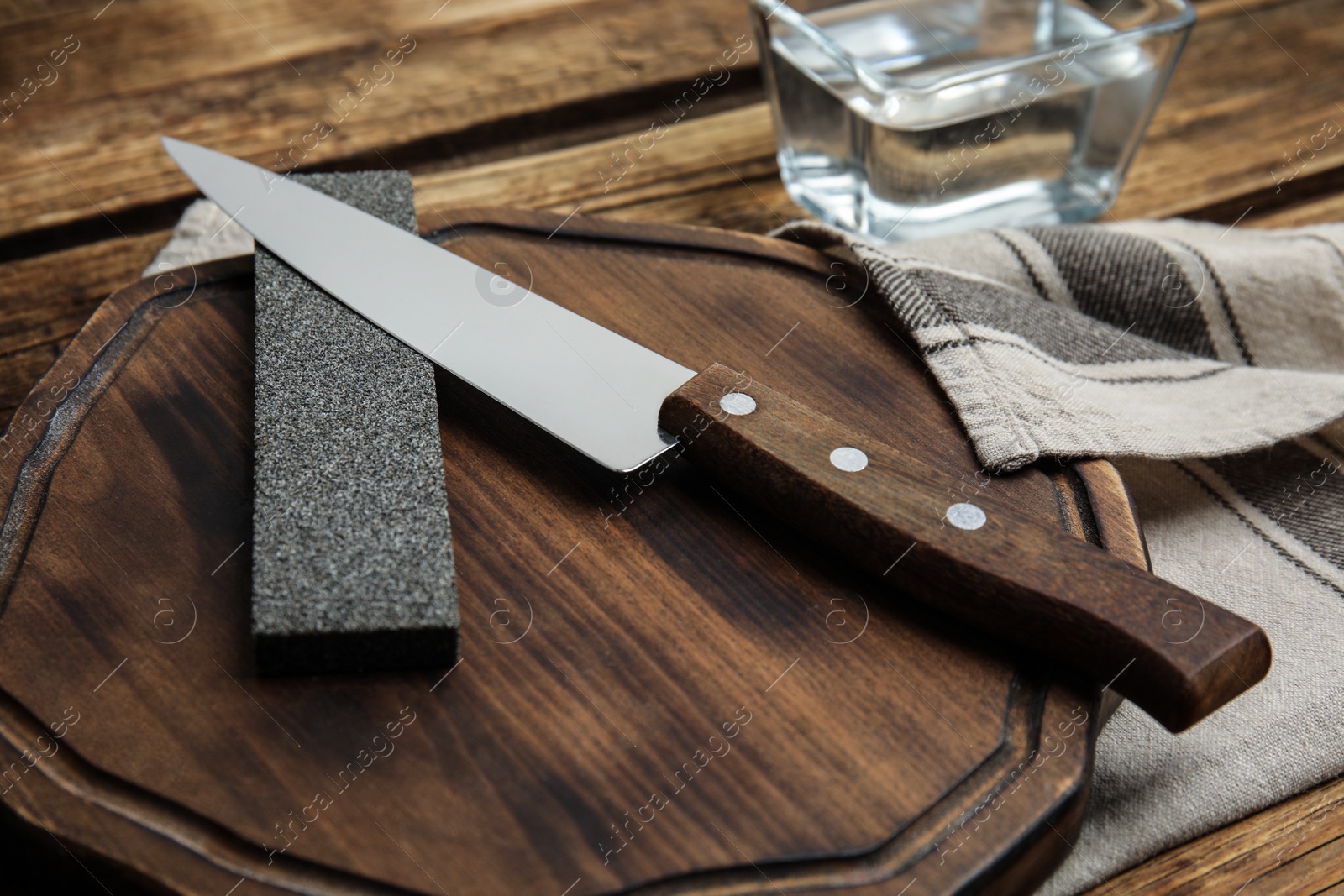 Photo of Sharpening stone and knife on wooden board, closeup