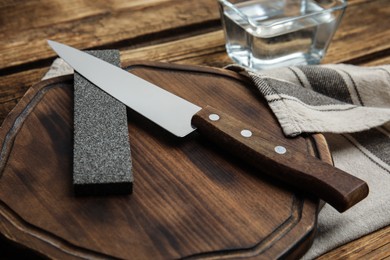 Photo of Sharpening stone and knife on wooden board, closeup