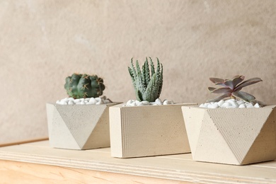 Beautiful succulent plants in stylish flowerpots on wooden table against brown background. Home decor