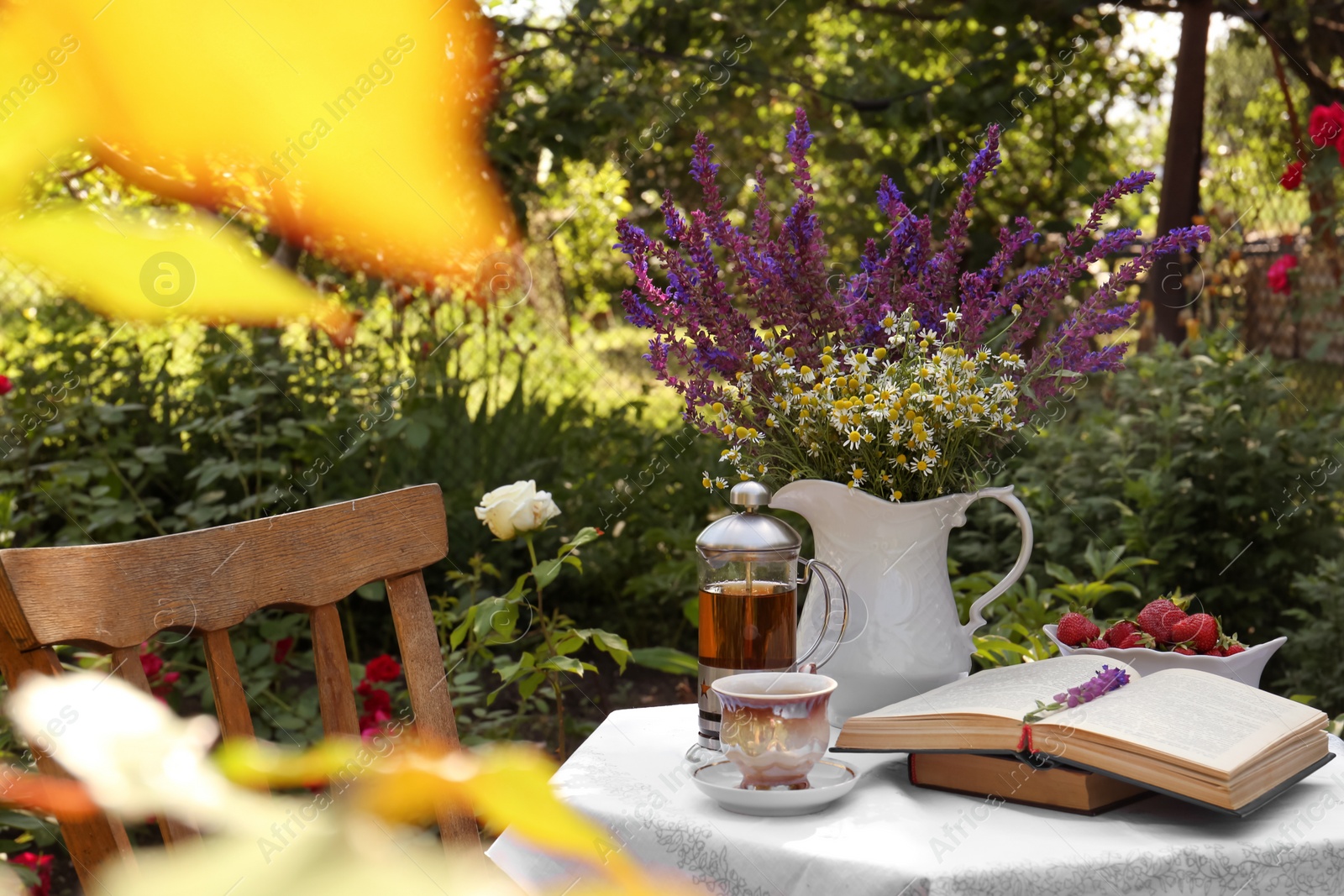 Photo of Beautiful bouquet of wildflowers and books on table served for tea drinking in garden