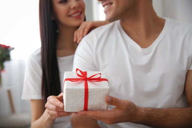 Photo of Man presenting gift to his beloved woman at home, focus on box. Valentine's day celebration