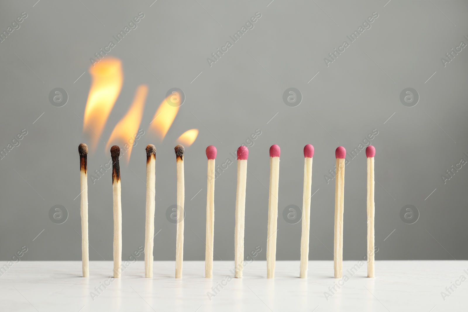 Photo of Line of burning and whole matches on table against grey background