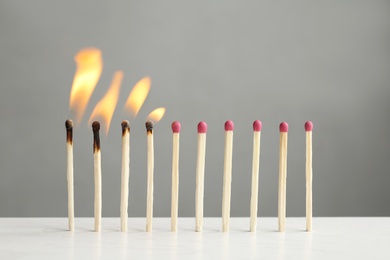 Line of burning and whole matches on table against grey background