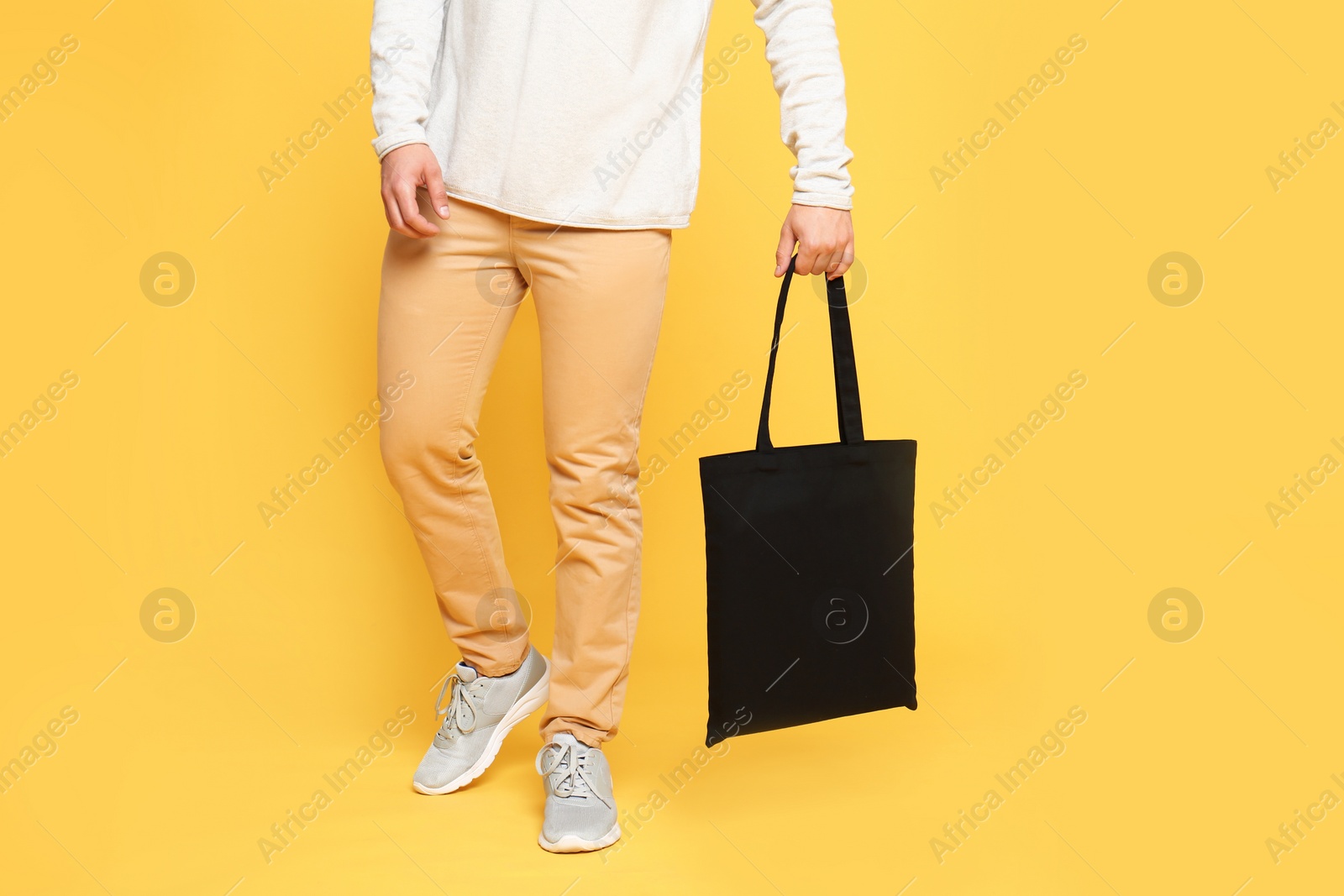 Photo of Young man with eco bag on yellow background, closeup